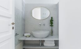 Modern bathroom design featuring a marble sink with an oval mirror, neatly arranged towels, and a decorative plant in a glass vase. The minimalist aesthetic is highlighted by clean lines and a light color palette, creating a serene atmosphere.