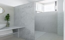 Modern bathroom featuring a sleek marble shower with a glass door, a minimalist sink, and a stylish mirror. Natural light streams in through an open window, enhancing the serene atmosphere. A decorative plant adds a touch of greenery to the elegant design.