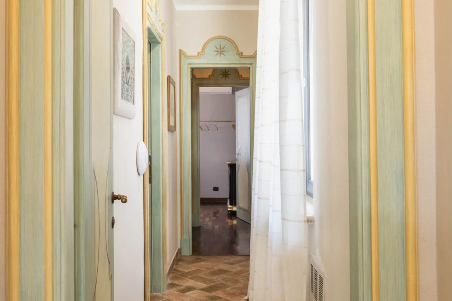 Interior view of a stylish hallway featuring light-colored walls with green and yellow accents, wooden flooring, and a bright window draped with sheer curtains. The hallway leads to additional rooms, showcasing decorative trim and artwork on the walls, creating an inviting and elegant atmosphere. | Only on SopranoVillas