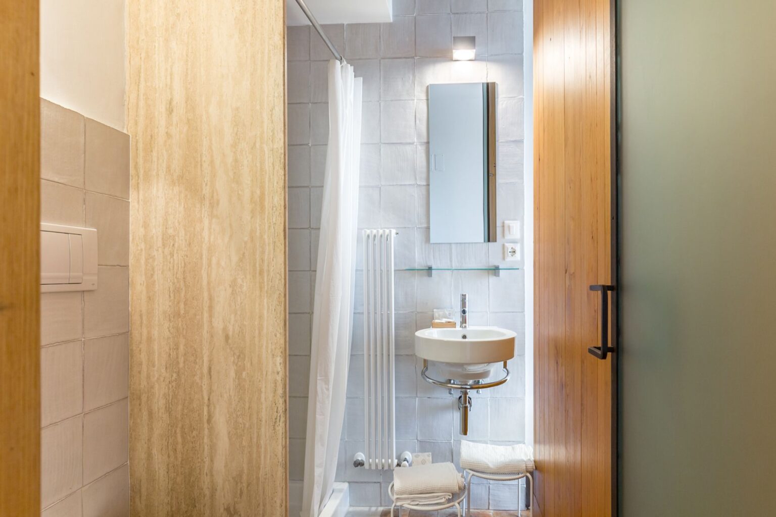 Modern bathroom interior featuring a sleek design with a glass shower, a round sink, a mirror, and stylish wooden accents. The space is bright and functional, showcasing contemporary tiles and efficient use of space. | Only on SopranoVillas
