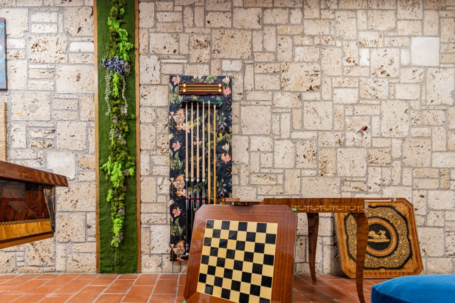 Interior view of a stylish game room featuring a stone wall, a vertical moss garden, and decorative game tables including a chessboard. The room combines natural elements with artistic decor, creating a cozy and inviting atmosphere. | Only on SopranoVillas
