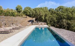 Modern infinity pool surrounded by lush greenery and stone pathways, featuring lounge chairs on a gravel patio, ideal for relaxation and outdoor enjoyment.