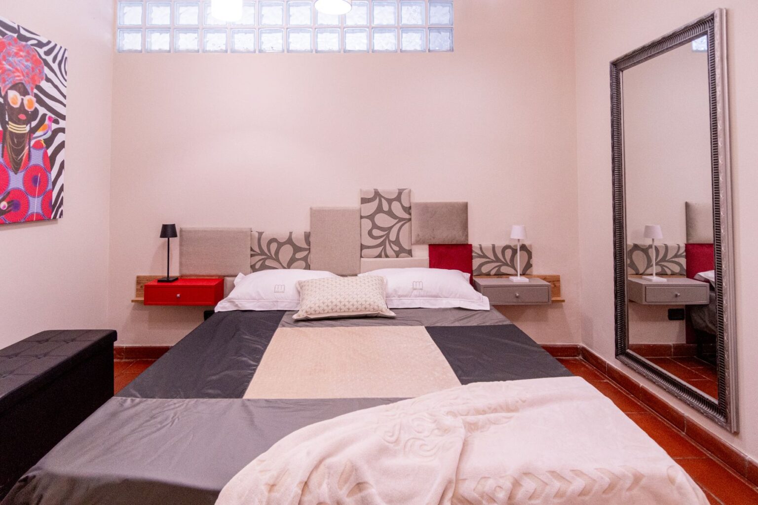 Modern bedroom interior featuring a large bed with decorative pillows, stylish headboard, and minimalist bedside tables. The room includes a full-length mirror, soft lighting, and vibrant artwork on the wall, creating a cozy and inviting atmosphere. | Only on SopranoVillas