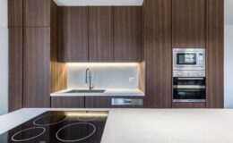 Modern kitchen with dark wood cabinetry, a sleek marble countertop, stainless steel appliances, and an integrated sink and stovetop. The design features under-cabinet lighting, enhancing the contemporary aesthetic.