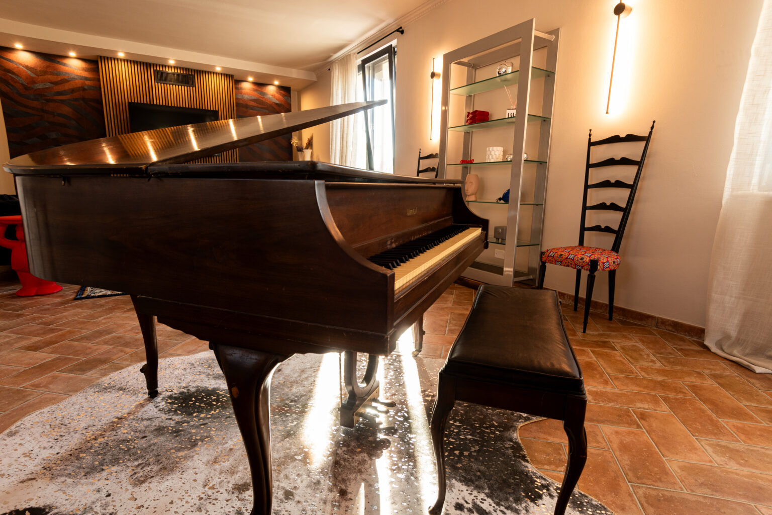 Grand piano in a stylish living room with modern decor, featuring a sleek design, a comfortable bench, and a decorative rug. The background includes a wall-mounted TV and a glass display shelf, enhancing the contemporary ambiance. | Only on SopranoVillas