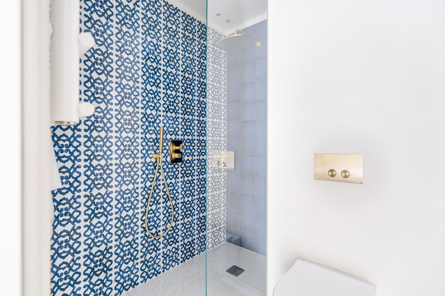 Modern bathroom shower with intricate blue and white patterned tiles, gold fixtures, and a glass enclosure, featuring a sleek showerhead and contemporary controls. | Only on SopranoVillas