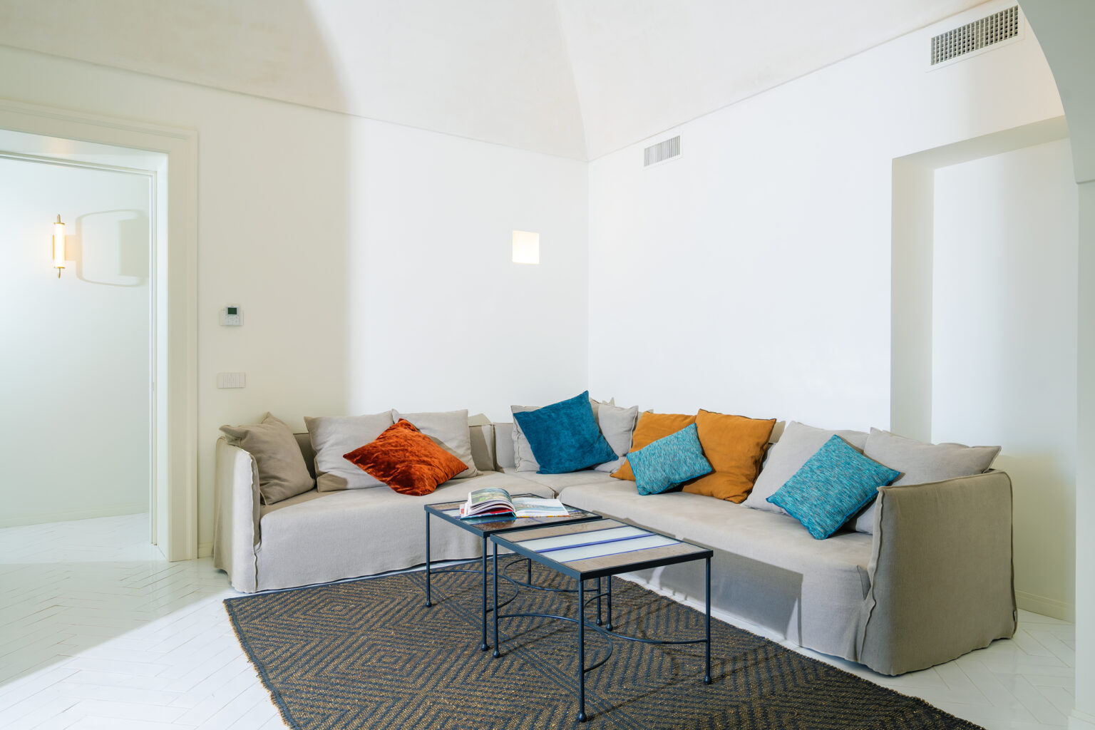 Cozy living room featuring a light-colored sofa adorned with colorful pillows, a modern coffee table, and a textured rug, all set against bright white walls and natural light. | Only on SopranoVillas