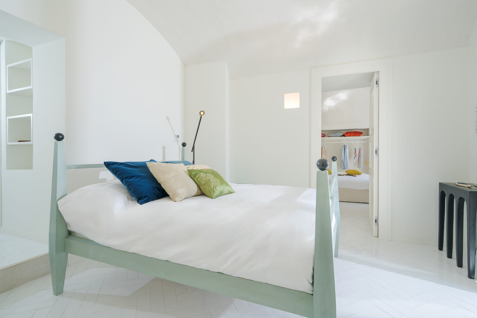 Bright and airy bedroom featuring a light green bed with decorative pillows, minimalist decor, and an adjacent closet area. The room showcases a contemporary design with white walls and herringbone patterned flooring, creating a serene atmosphere. | Only on SopranoVillas