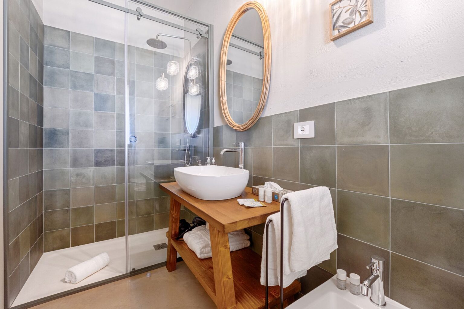 Modern bathroom featuring a glass shower enclosure, stylish wooden vanity with a round mirror, and essential toiletries. The design incorporates neutral tile colors and natural materials for a contemporary and calming atmosphere. | Only on SopranoVillas