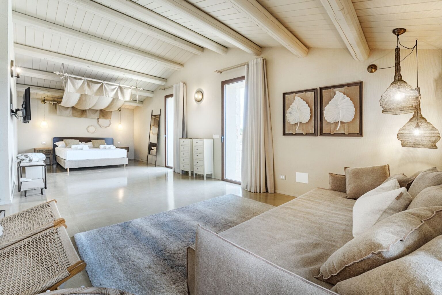 Spacious modern bedroom featuring a king-sized bed, stylish decor with natural tones, and a cozy seating area. The room includes large windows for natural light, elegant pendant lights, and tasteful wall art, creating a serene atmosphere. Ideal for relaxation and comfort in a contemporary setting. | Only on SopranoVillas