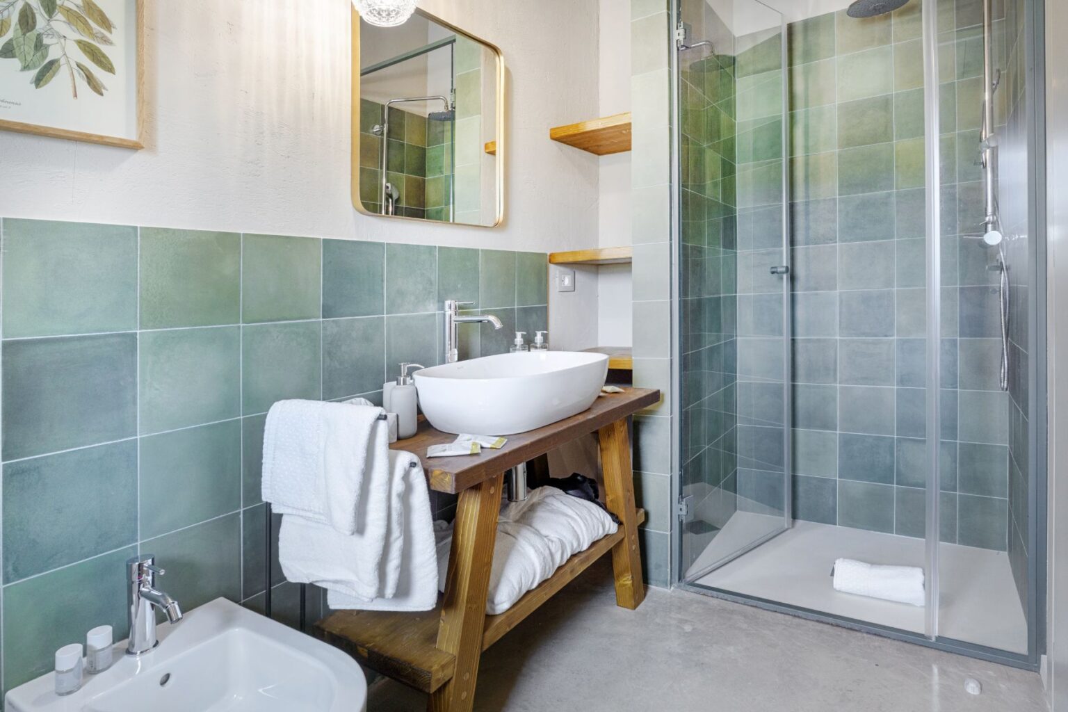 Modern bathroom featuring a stylish green tiled wall, a wooden vanity with a white basin, neatly arranged towels, and a glass shower enclosure, creating a fresh and relaxing atmosphere. | Only on SopranoVillas