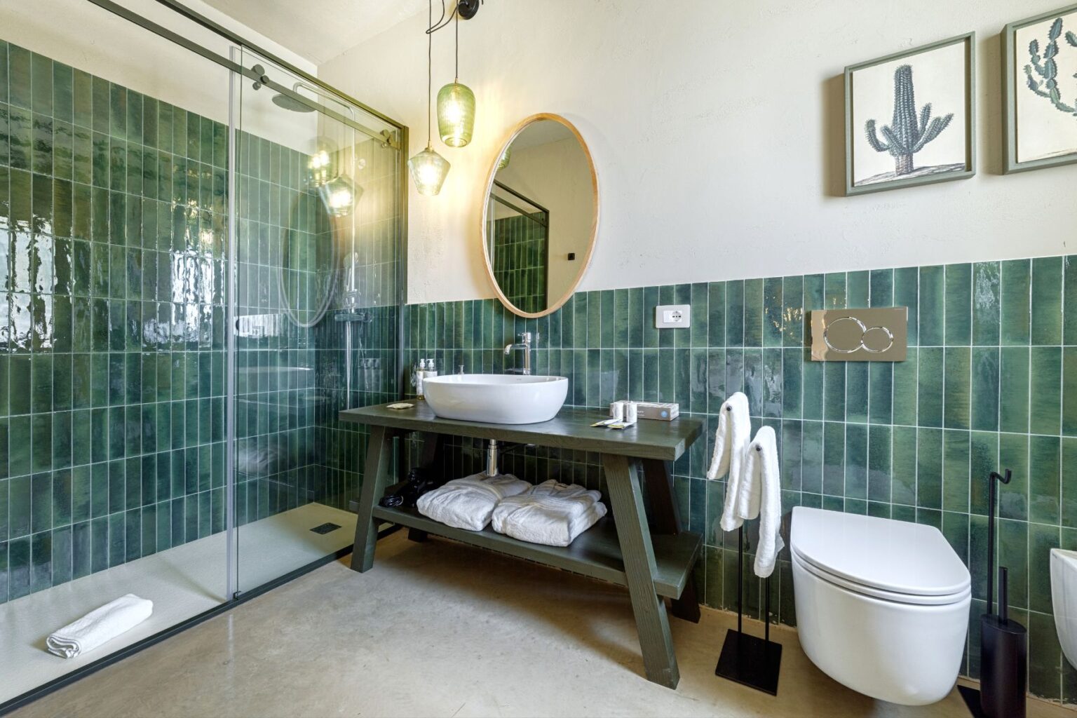 Modern bathroom featuring green tiled walls, a stylish shower area, a circular mirror, a wall-mounted sink, and decorative plants. Elegantly designed with natural light and minimalist fixtures, creating a spa-like atmosphere. | Only on SopranoVillas