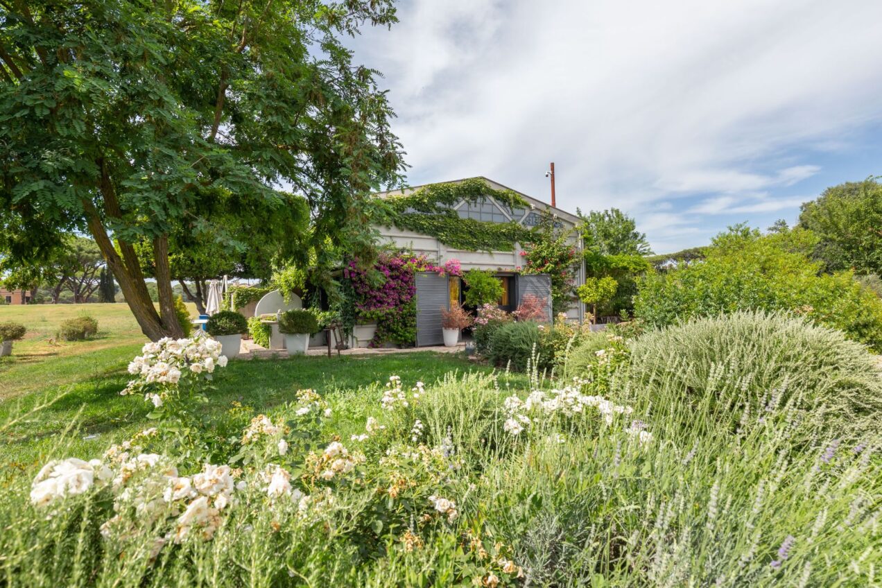 Charming countryside home surrounded by vibrant gardens, featuring blooming flowers and lush greenery under a clear blue sky. Ideal for nature lovers and those seeking a peaceful retreat. | Only on SopranoVillas