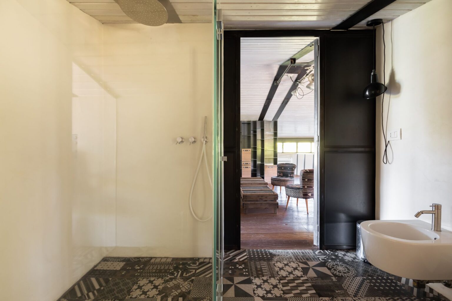 Modern bathroom interior featuring a glass shower enclosure, stylish patterned floor tiles, and a sleek sink. The open layout connects to a living area with wooden furniture and natural light. | Only on SopranoVillas