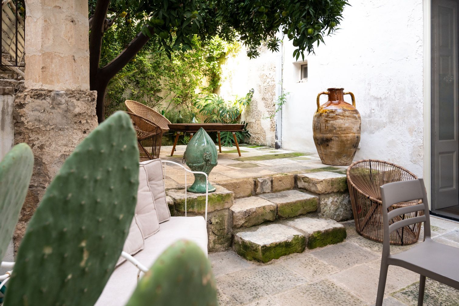 Charming outdoor garden space featuring stone steps, greenery, and rustic decor, including a large clay pot and stylish wicker furniture, ideal for relaxation and outdoor gatherings. | Only on SopranoVillas
