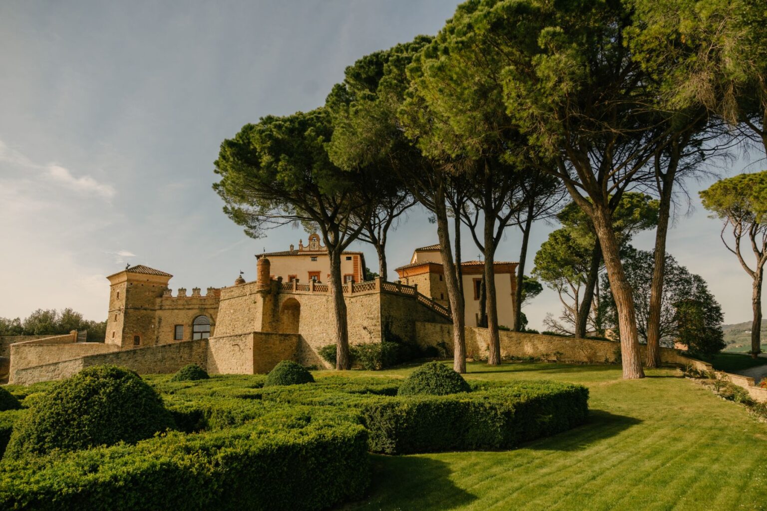 Historic Italian castle surrounded by manicured gardens and tall trees, showcasing a picturesque landscape under a clear sky. Ideal for travel and architectural photography. | Only on SopranoVillas