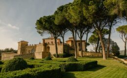 Historic Italian castle surrounded by manicured gardens and tall trees, showcasing a picturesque landscape under a clear sky. Ideal for travel and architectural photography.
