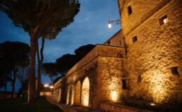Historic stone building illuminated at night, featuring arched windows and a cobblestone path lined with trees and lamps. Ideal for showcasing architectural beauty and evening ambiance in outdoor settings.