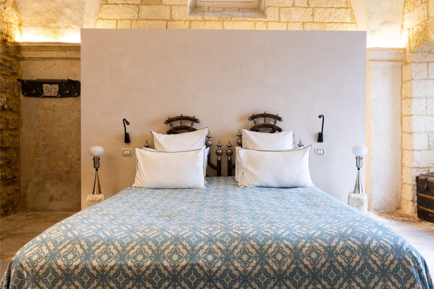 Cozy bedroom featuring a stylish bed with decorative pillows, an intricate patterned bedspread, and unique wall sconces. The rustic stone walls and elegant design elements create a warm and inviting atmosphere. | Only on SopranoVillas