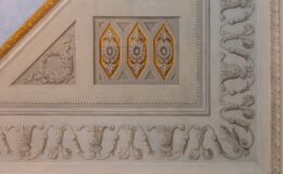 Intricate ceiling design featuring ornate plasterwork, decorative floral motifs, and diamond-shaped panels with gold accents, showcasing classical architectural details.