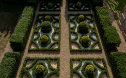 Symmetrical formal garden design featuring manicured hedges, circular topiary, and gravel pathways, showcasing intricate patterns and lush greenery.
