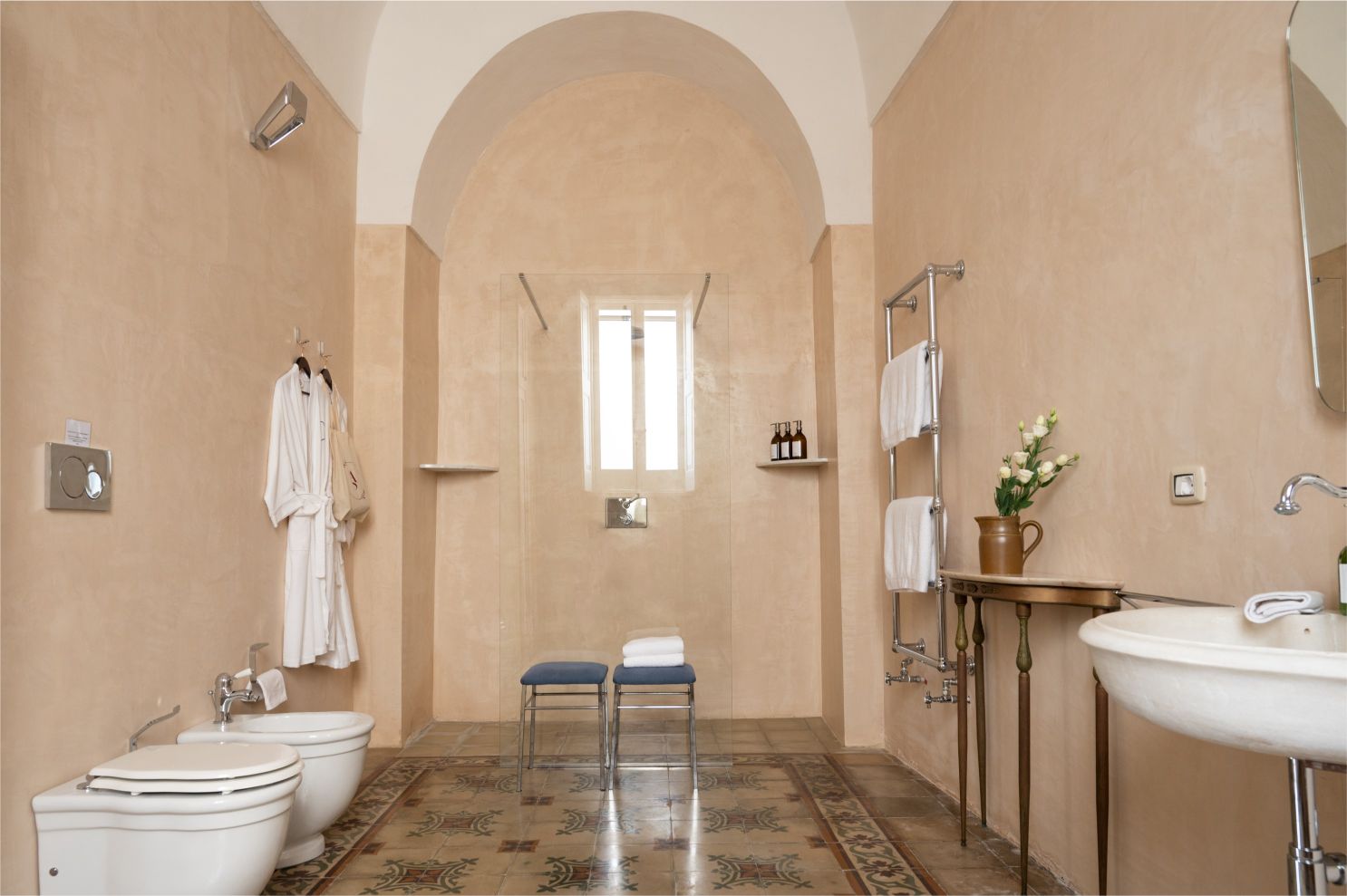 Spacious and modern bathroom featuring a walk-in shower, elegant fixtures, and decorative tiled flooring. The room includes a stylish sink, a towel rack, and a seating area, creating a serene and inviting atmosphere. | Only on SopranoVillas