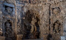 Interior view of a historic grotto featuring intricate rock formations and sculptures, including a central mermaid figure and decorative carvings of mythical creatures, showcasing unique architectural details and textures.
