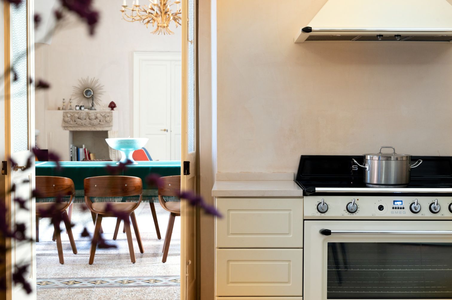 Modern kitchen interior featuring a sleek SMEG oven, a stainless steel pot on the stove, and a view into an elegant dining area with wooden chairs and a decorative bowl on the table. Soft lighting and stylish decor create a warm atmosphere. | Only on SopranoVillas