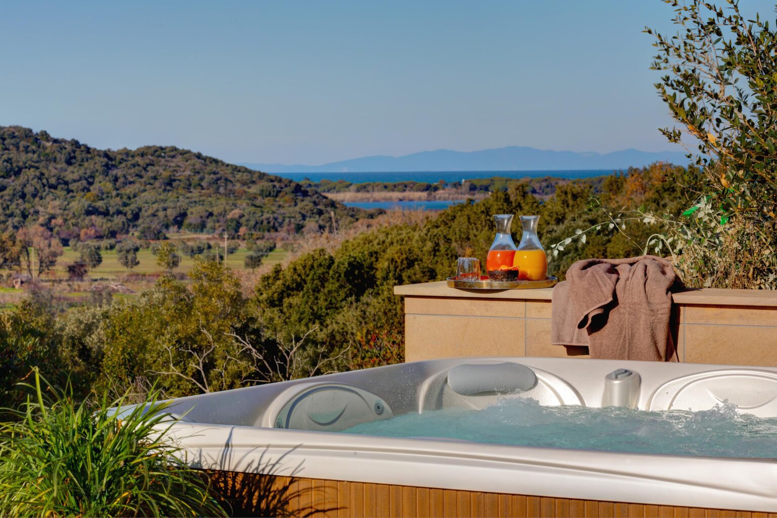 Relaxing outdoor hot tub with a scenic view of mountains and a lake, complemented by a tray of refreshing drinks and a towel nearby, perfect for a tranquil getaway. | Only on SopranoVillas