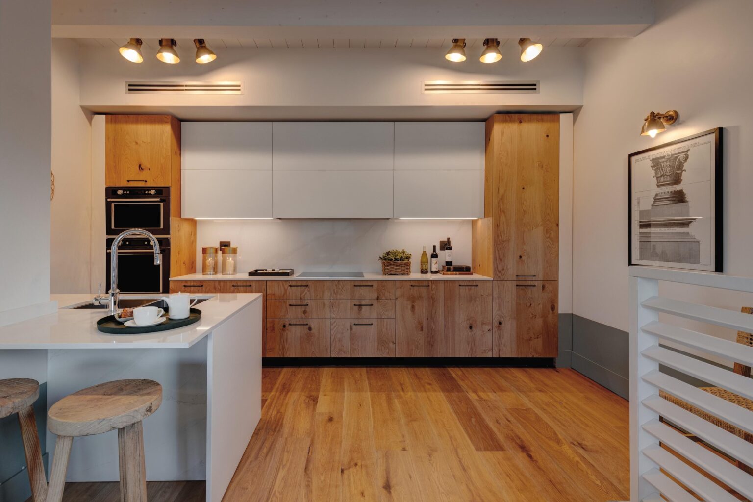 Modern kitchen featuring a blend of white and wooden cabinetry, stainless steel appliances, and a sleek countertop. The space is enhanced by warm lighting and natural wood flooring, creating a stylish and inviting atmosphere. | Only on SopranoVillas