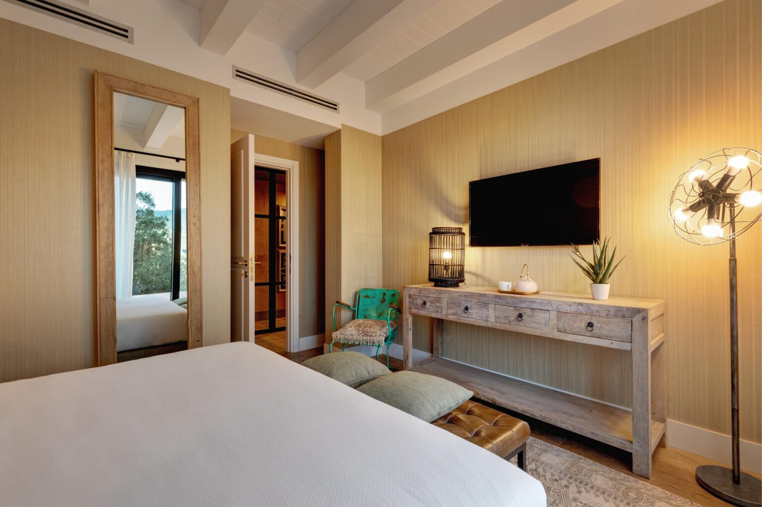 Modern bedroom interior featuring a large mirror, wooden console table, flat-screen TV, and stylish lighting. The room is decorated with neutral tones and natural elements, creating a cozy and inviting atmosphere. | Only on SopranoVillas