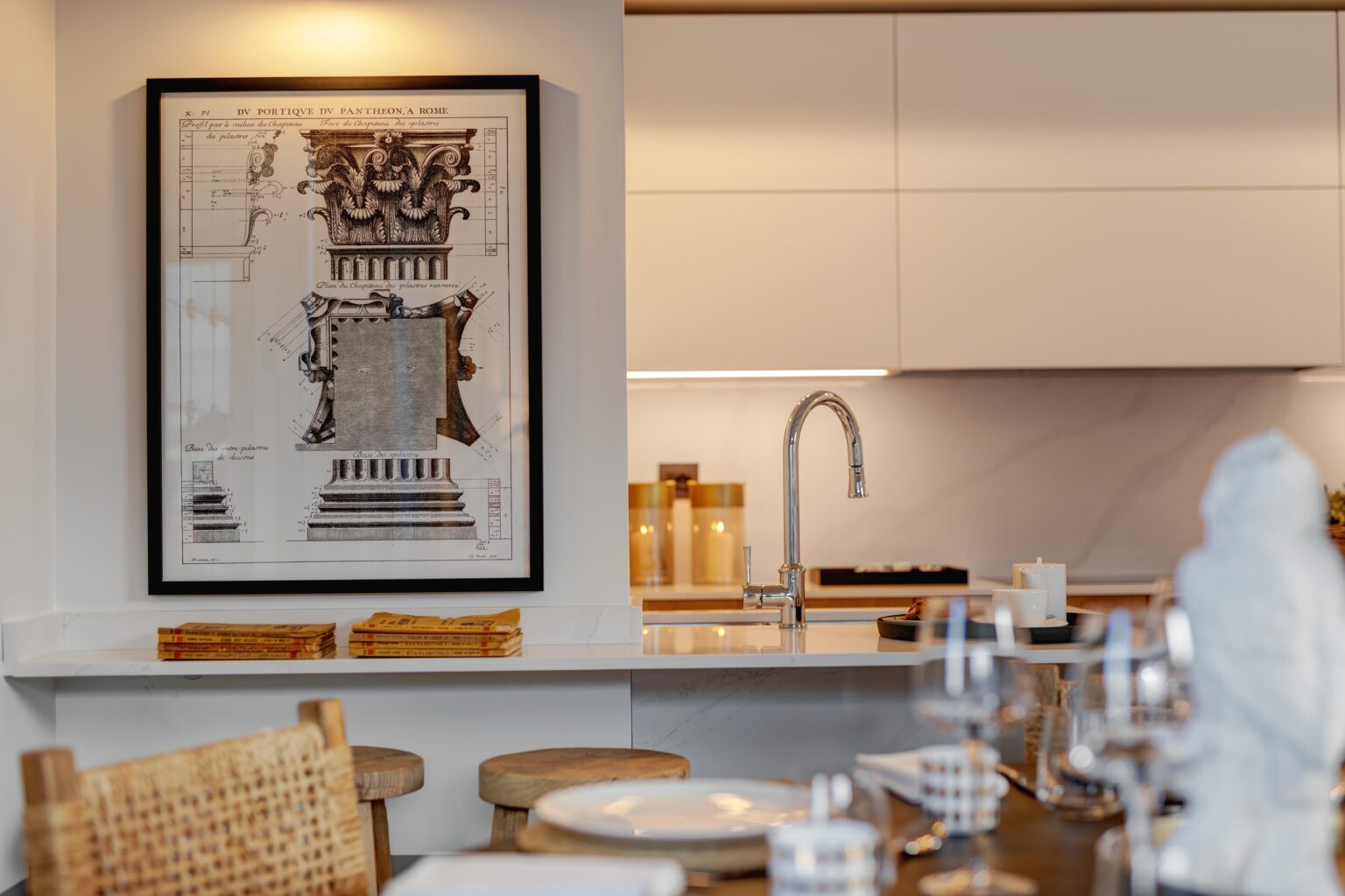 Stylish kitchen interior featuring a vintage architectural print of a Roman column, modern cabinetry, and a sleek faucet. Wooden stools and tableware are arranged for an inviting dining experience. | Only on SopranoVillas