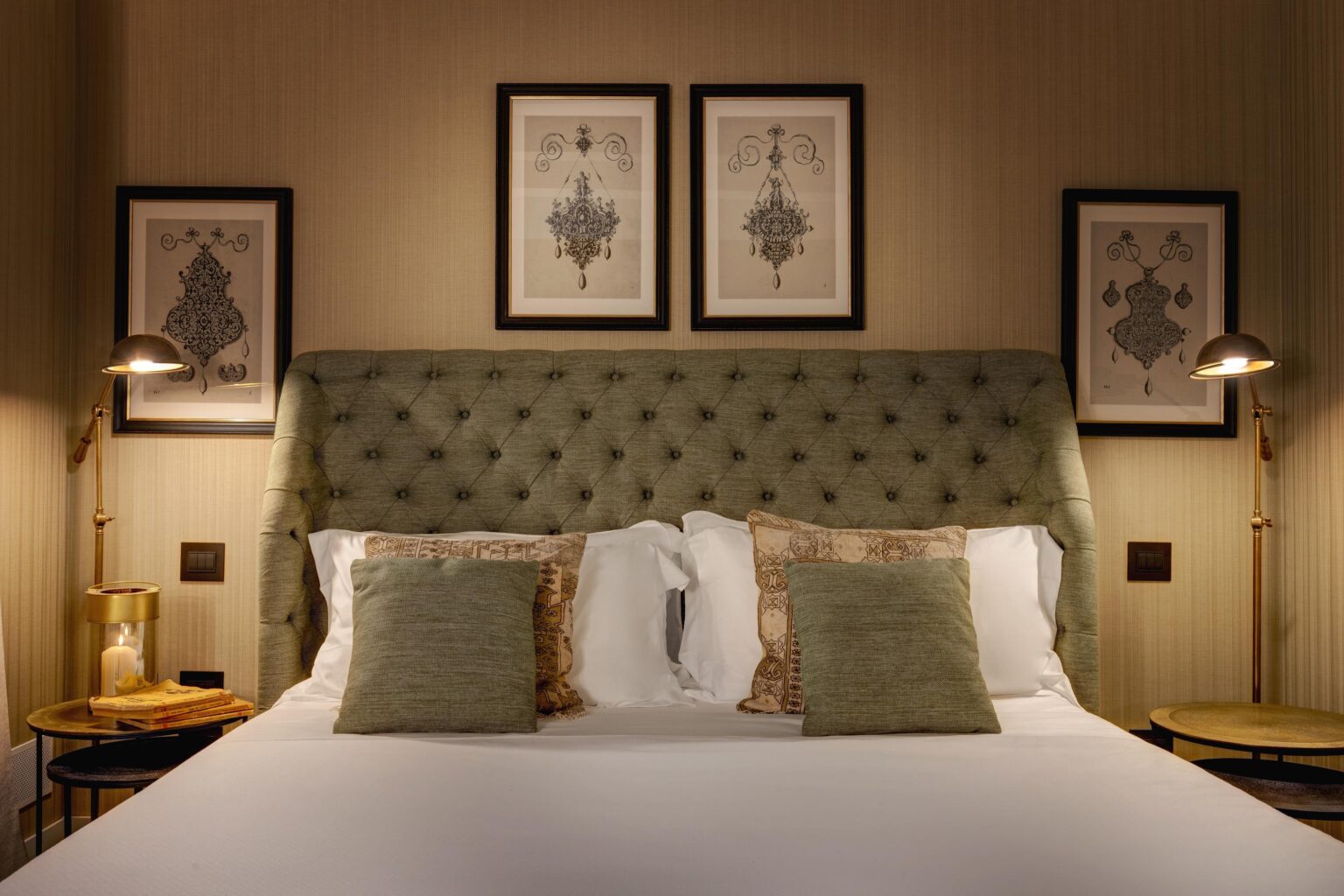Cozy hotel bedroom featuring a tufted green headboard, decorative pillows, and elegant wall art. A stylish bedside lamp and small table complement the sophisticated decor, creating a relaxing atmosphere. | Only on SopranoVillas