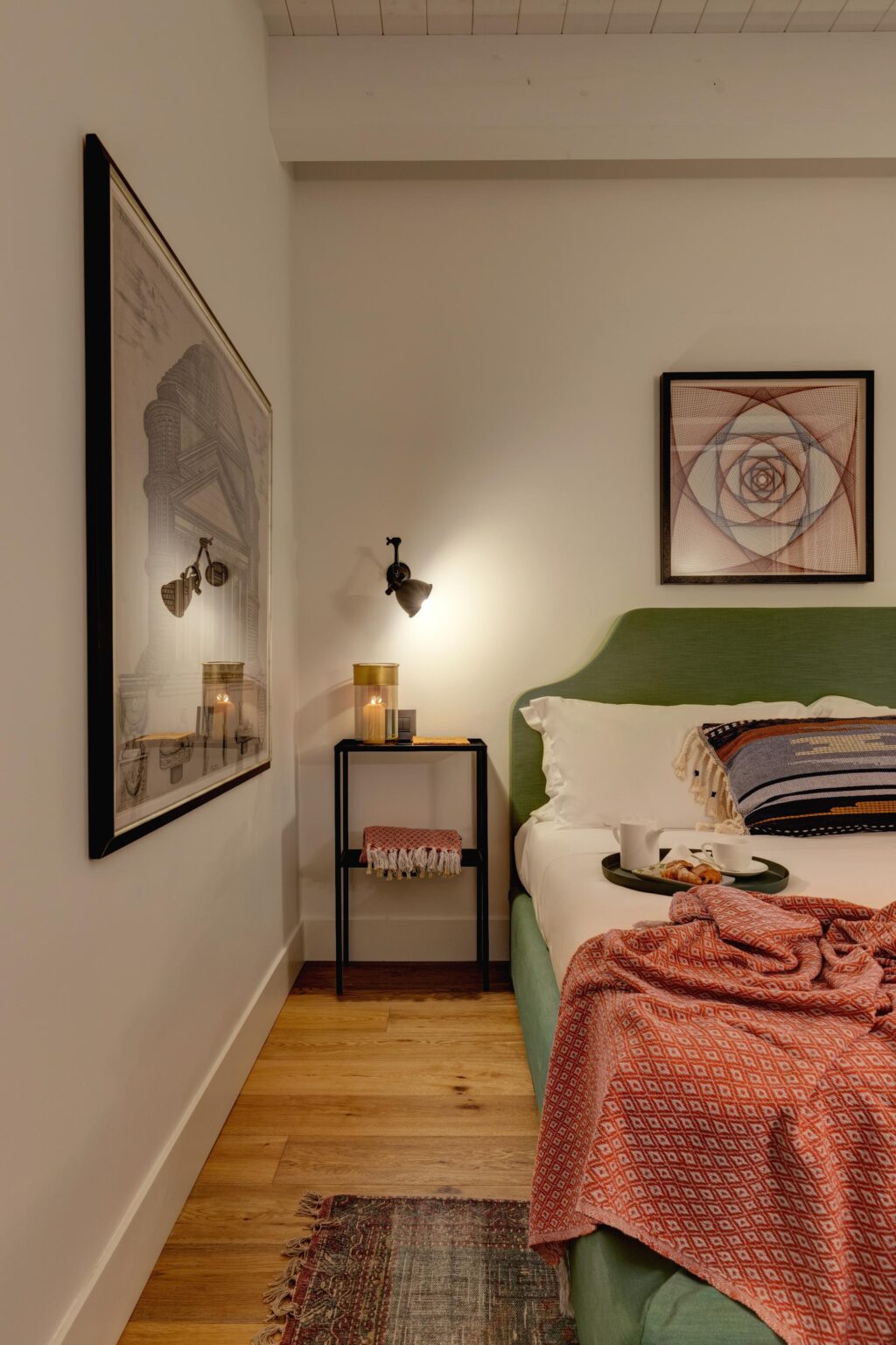 Cozy bedroom interior featuring a green upholstered headboard, a decorative orange blanket, and a stylish nightstand with candles. The room is adorned with framed artwork and a patterned rug, creating a warm and inviting atmosphere. | Only on SopranoVillas