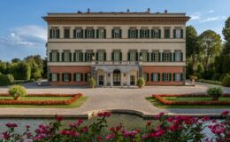 Elegant villa with green shutters surrounded by manicured gardens and colorful flower beds, reflecting classic architectural design under a clear blue sky.