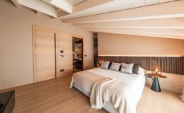 Modern bedroom interior featuring a cozy bed with decorative pillows, a stylish bedside table with a lamp, and warm lighting. The design includes wooden accents, neutral color tones, and a spacious layout, creating a serene and inviting atmosphere. Ideal for relaxation and comfort.