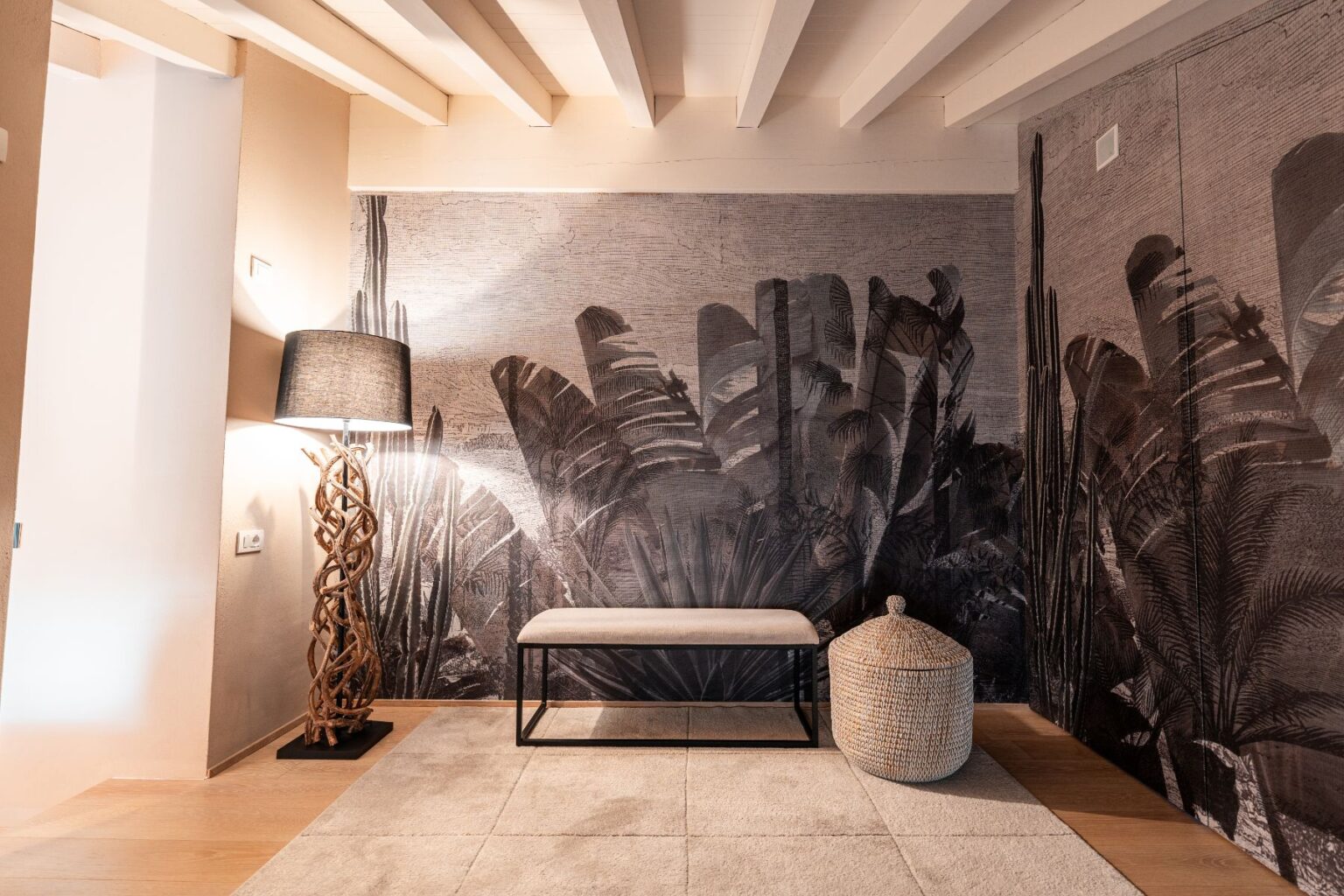 Stylish interior featuring a textured wall mural of tropical plants, a modern bench, a woven storage basket, and a unique wooden lamp. The warm lighting and natural elements create a cozy atmosphere. | Only on SopranoVillas
