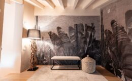 Stylish interior featuring a textured wall mural of tropical plants, a modern bench, a woven storage basket, and a unique wooden lamp. The warm lighting and natural elements create a cozy atmosphere.