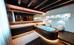 Modern luxury bathroom featuring a freestanding tub, dual sinks, and ambient LED lighting. The design incorporates natural wood and stone elements, with large windows allowing natural light to enhance the serene atmosphere.