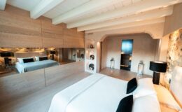 Modern bedroom interior featuring a spacious layout with a large bed, stylish decor, and wooden beams. The room includes mirrored walls, soft lighting, and elegant furnishings, creating a serene and inviting atmosphere. Perfect for a contemporary home design or hotel showcase.