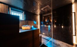 Modern spa bathroom featuring a glass shower, wooden sauna, and ambient lighting. Soft towels are neatly arranged on a wooden bench, creating a serene and luxurious atmosphere for relaxation.