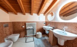 Modern bathroom interior featuring wooden beams, dual sinks, a stylish mirror, and a cozy atmosphere. The design includes a heated towel rack, decorative towels, and a woven basket, creating a functional and aesthetic space.