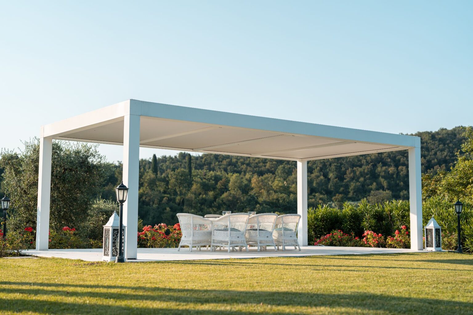 Modern outdoor pergola with white furniture set, surrounded by lush greenery and colorful flowers, ideal for relaxation and gatherings. | Only on SopranoVillas
