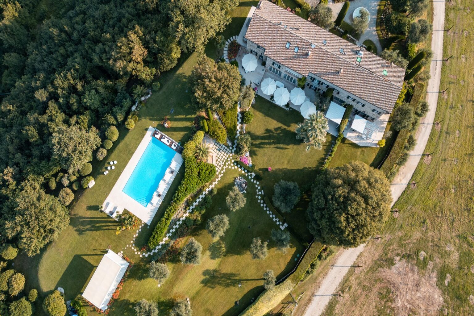Aerial view of a luxurious villa featuring a swimming pool surrounded by landscaped gardens, pathways, and outdoor seating areas, set amidst lush greenery. | Only on SopranoVillas