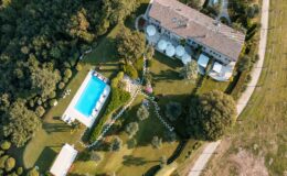 Aerial view of a luxurious villa featuring a swimming pool surrounded by landscaped gardens, pathways, and outdoor seating areas, set amidst lush greenery.