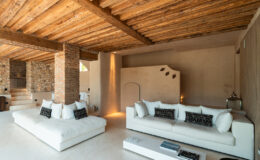 Modern living room featuring white sofas with black accent pillows, a minimalist coffee table, and exposed wooden beams. The interior design combines natural stone and smooth surfaces, creating a stylish and inviting atmosphere.