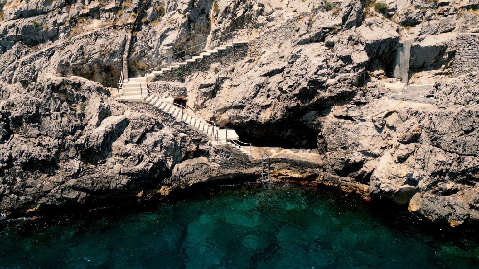 Stairs leading down rocky cliffs to clear turquoise water, showcasing a scenic coastal landscape. | Only on SopranoVillas