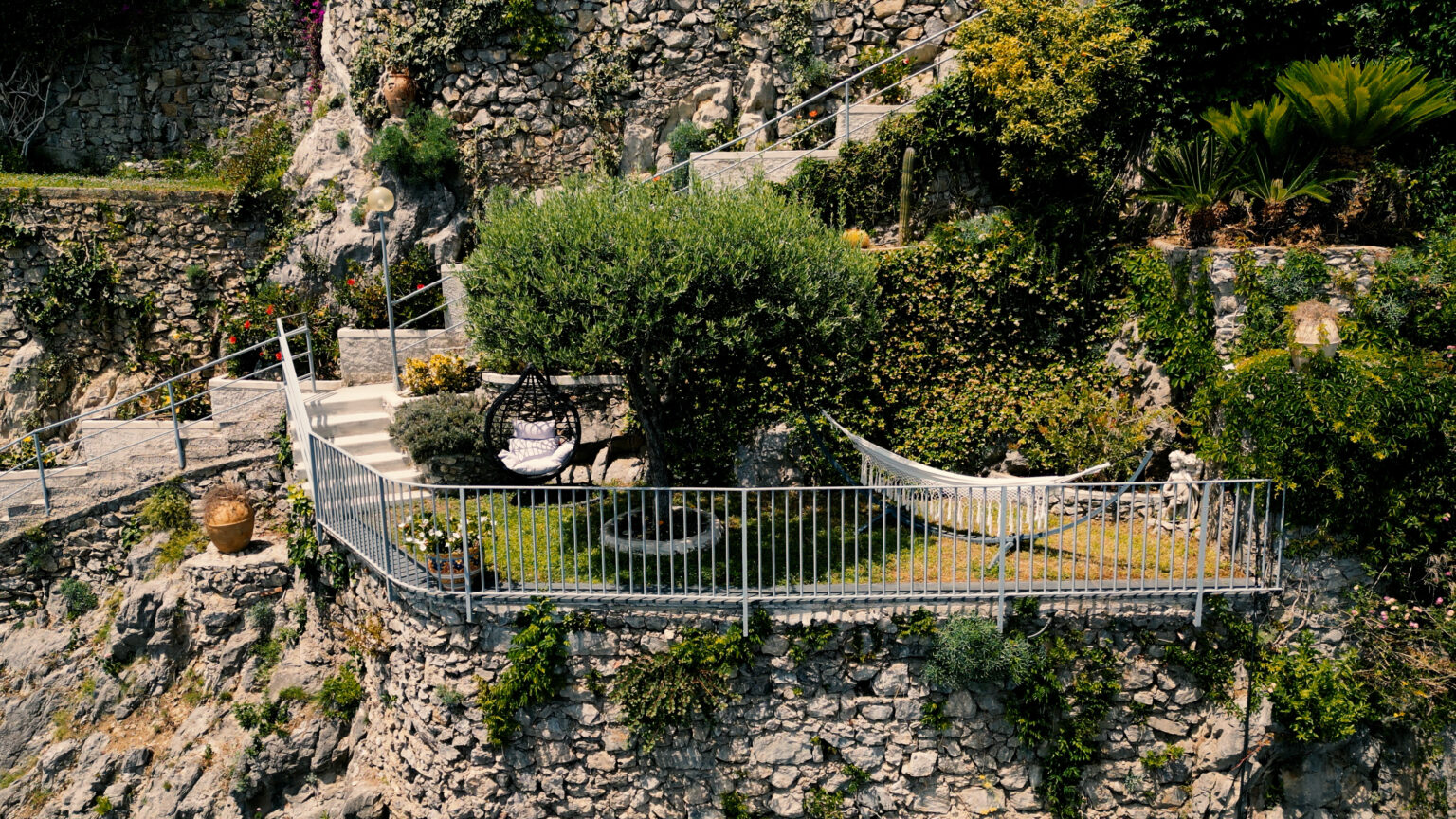 Aerial view of a tranquil outdoor patio with a hammock, surrounded by lush greenery and stone walls, featuring a cozy seating area and decorative plants. | Only on SopranoVillas