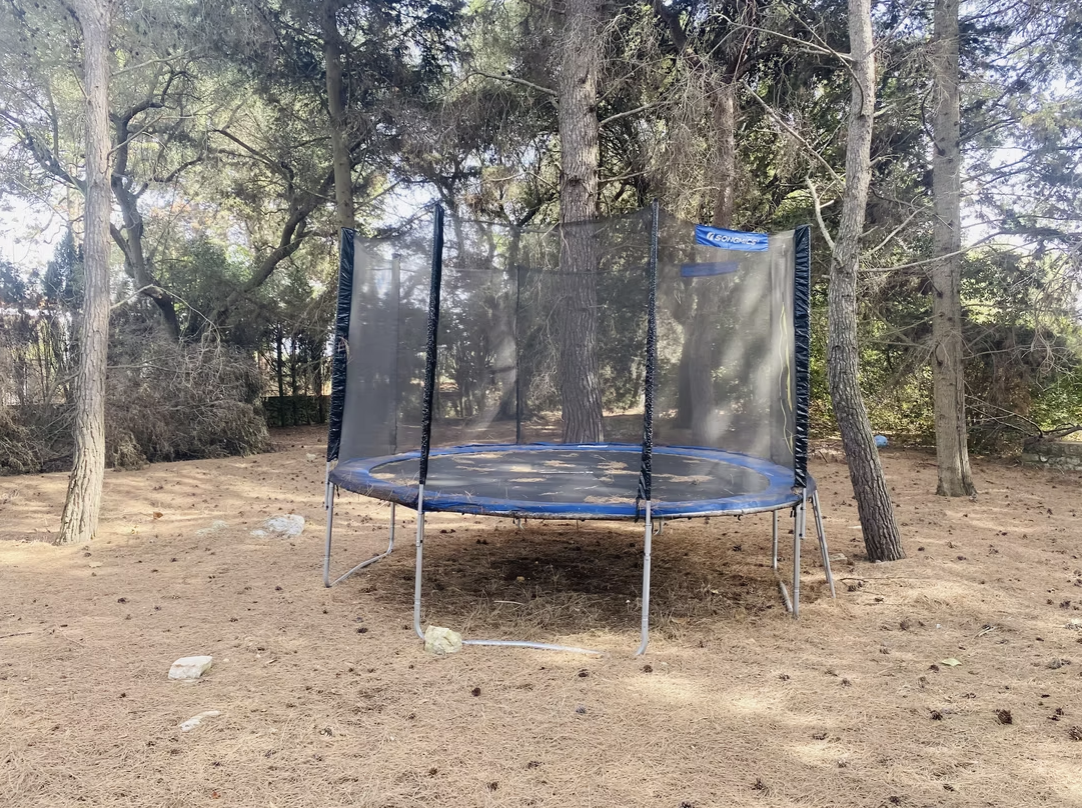 Trampoline surrounded by trees in a natural outdoor setting, featuring a safety enclosure and a sandy ground. Ideal for outdoor recreation and family fun. | Only on SopranoVillas
