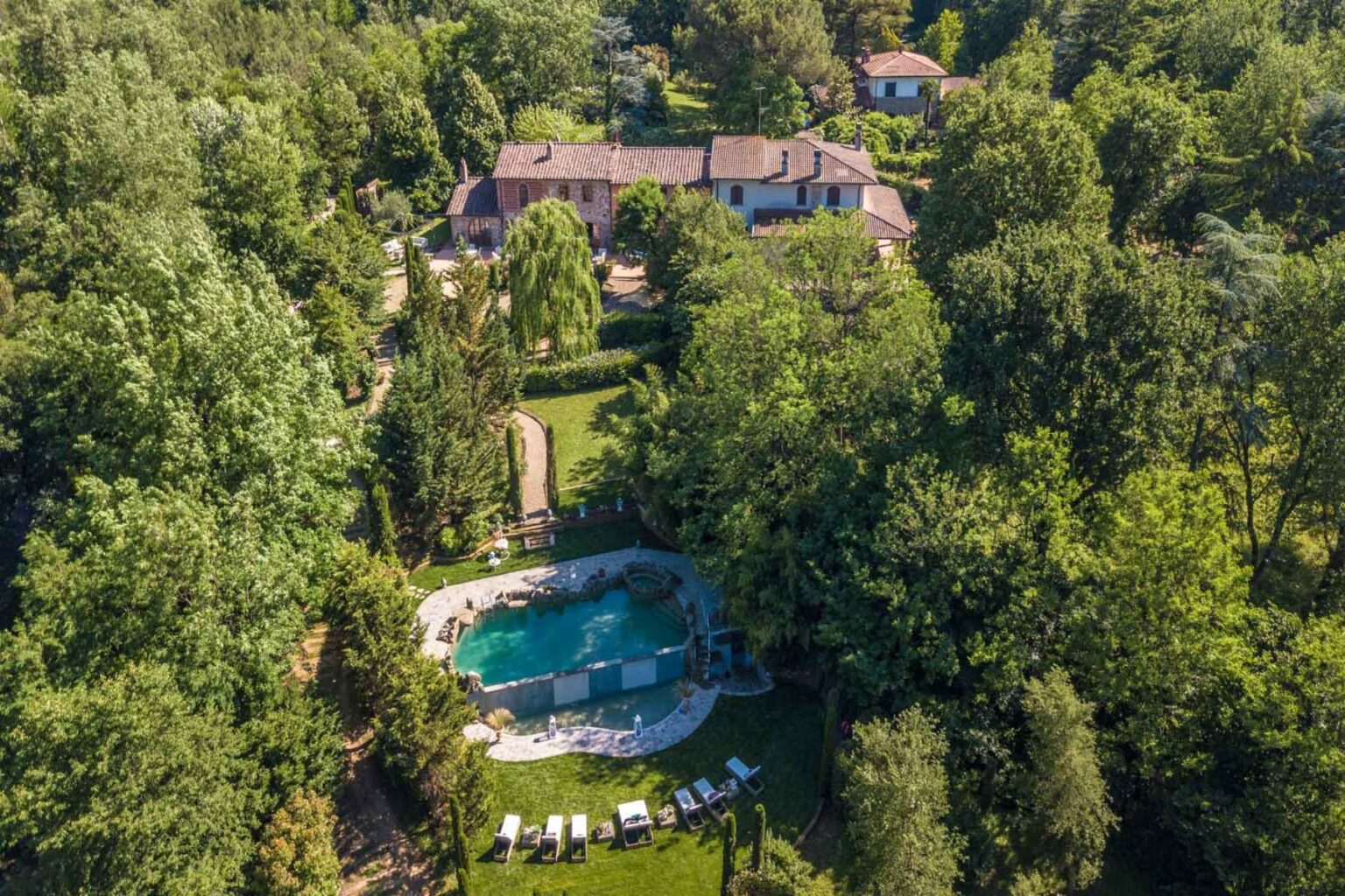 Aerial view of a luxurious villa surrounded by lush greenery, featuring a serene swimming pool and sun loungers in a tranquil garden setting. Perfect for relaxation and outdoor gatherings. | Only on SopranoVillas